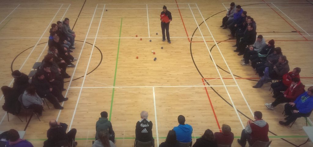 View from up high of court w3ith boccia balls in middle and people sitting around.