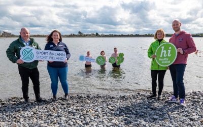 People standing on shore of lake holding signs promoting outdoor swimming.